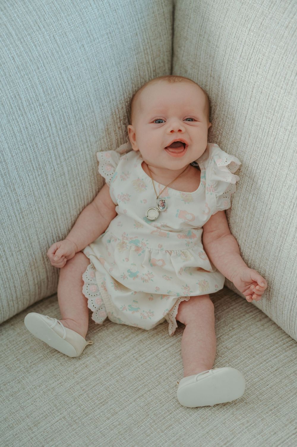 A baby in a floral onesie sits on a light gray couch, shown in a series of candid poses.