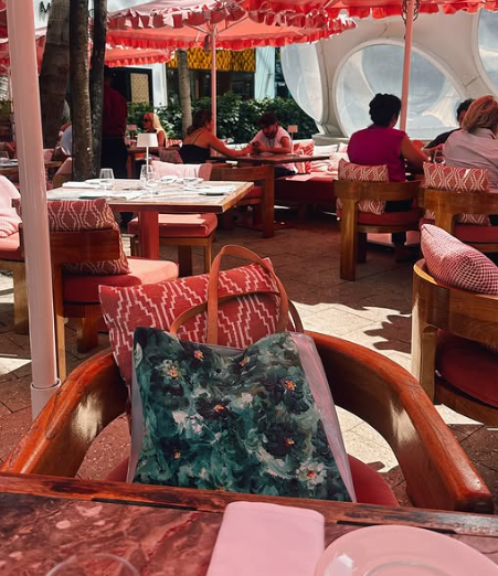A beachside restaurant with red umbrellas and cushioned seating areas creates a relaxing coastal dining atmosphere.