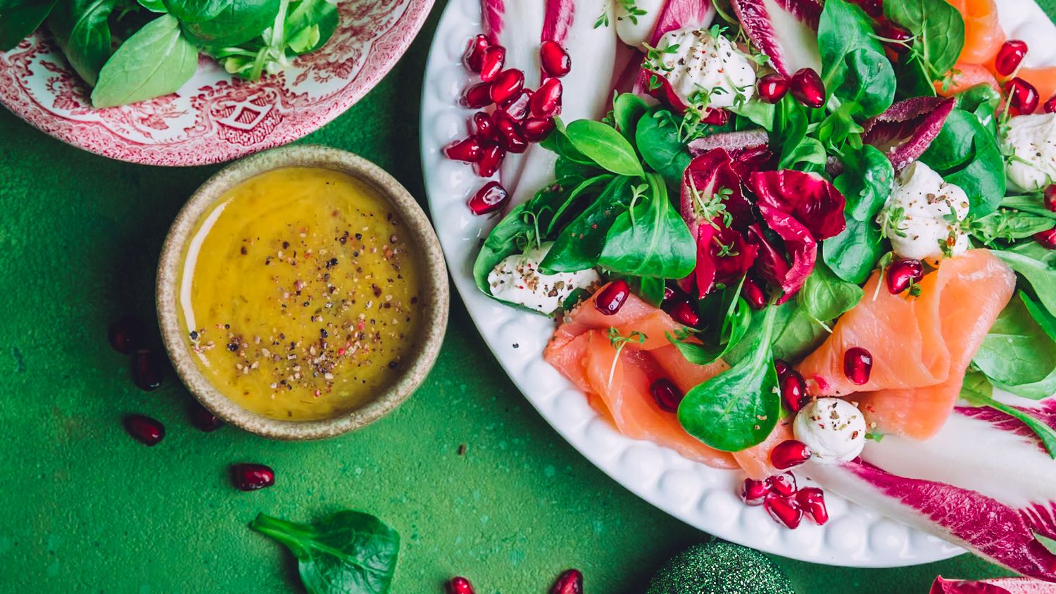 Fresh green peas and mint leaves scattered around a creamy pea puree in dark bowls on a black surface.
