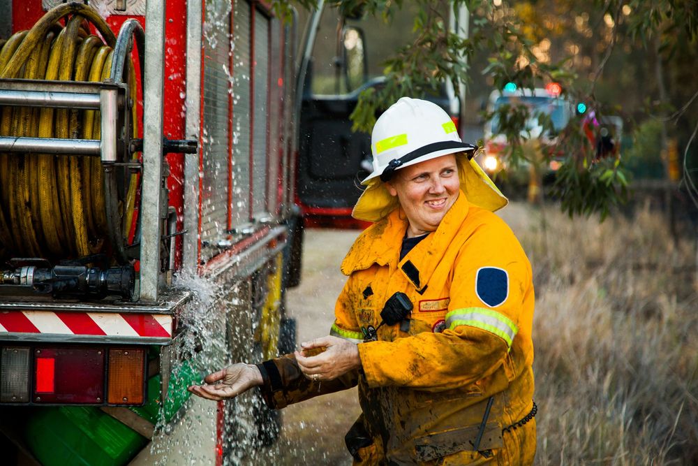A firefighter in yellow protective gear operates a water hose during a training exercise or emergency response.