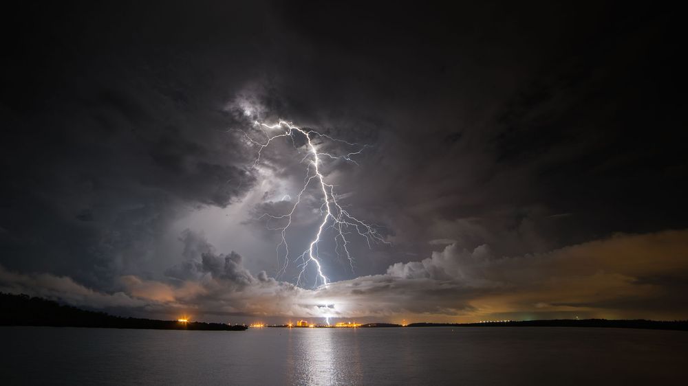 Dramatic lightning bolts illuminate the dark stormy sky over a vast desert landscape at night.