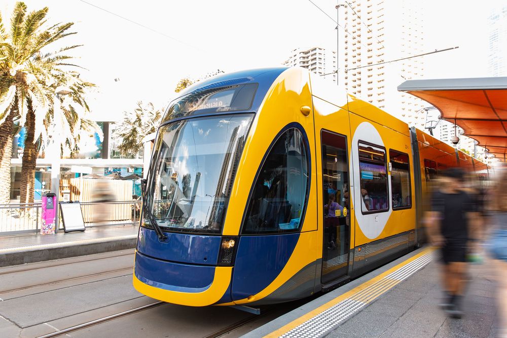 Modern commuter trains in yellow and blue livery wait at station platforms during daytime service.