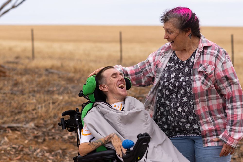 A heartwarming moment between two people sharing laughter in a rural field with brown grass and fencing in the background.