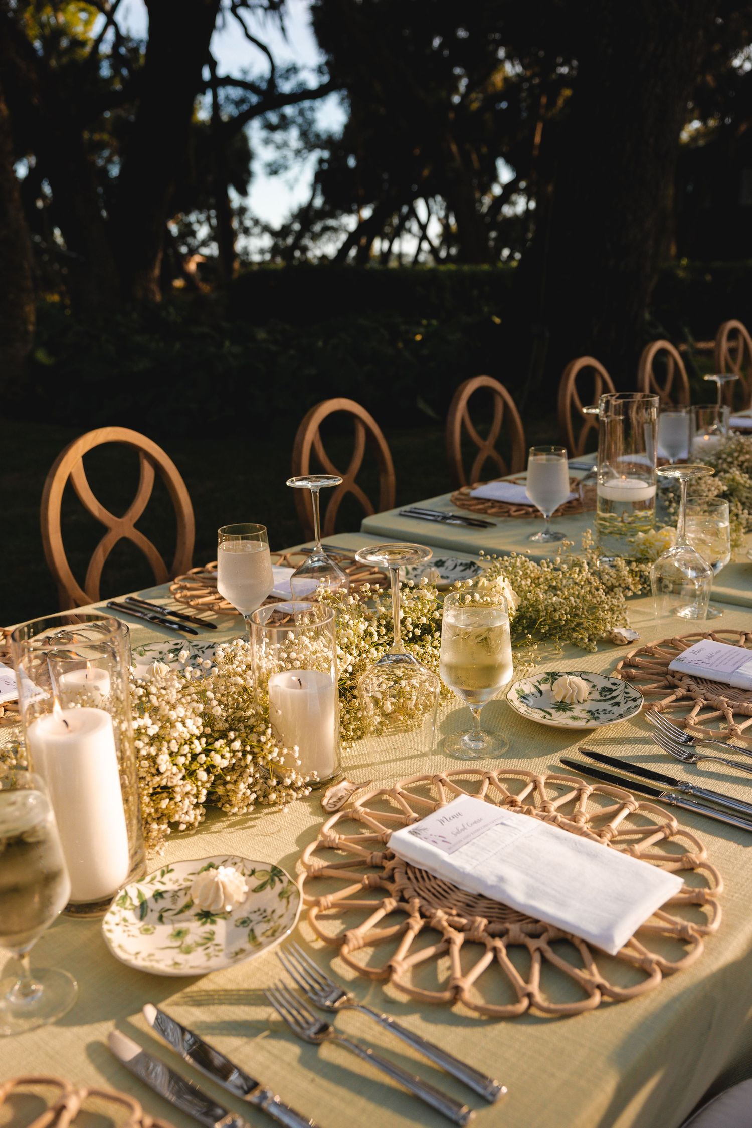 Elegant outdoor wedding table setting with candlelight and baby's breath garland decorations at dusk.
