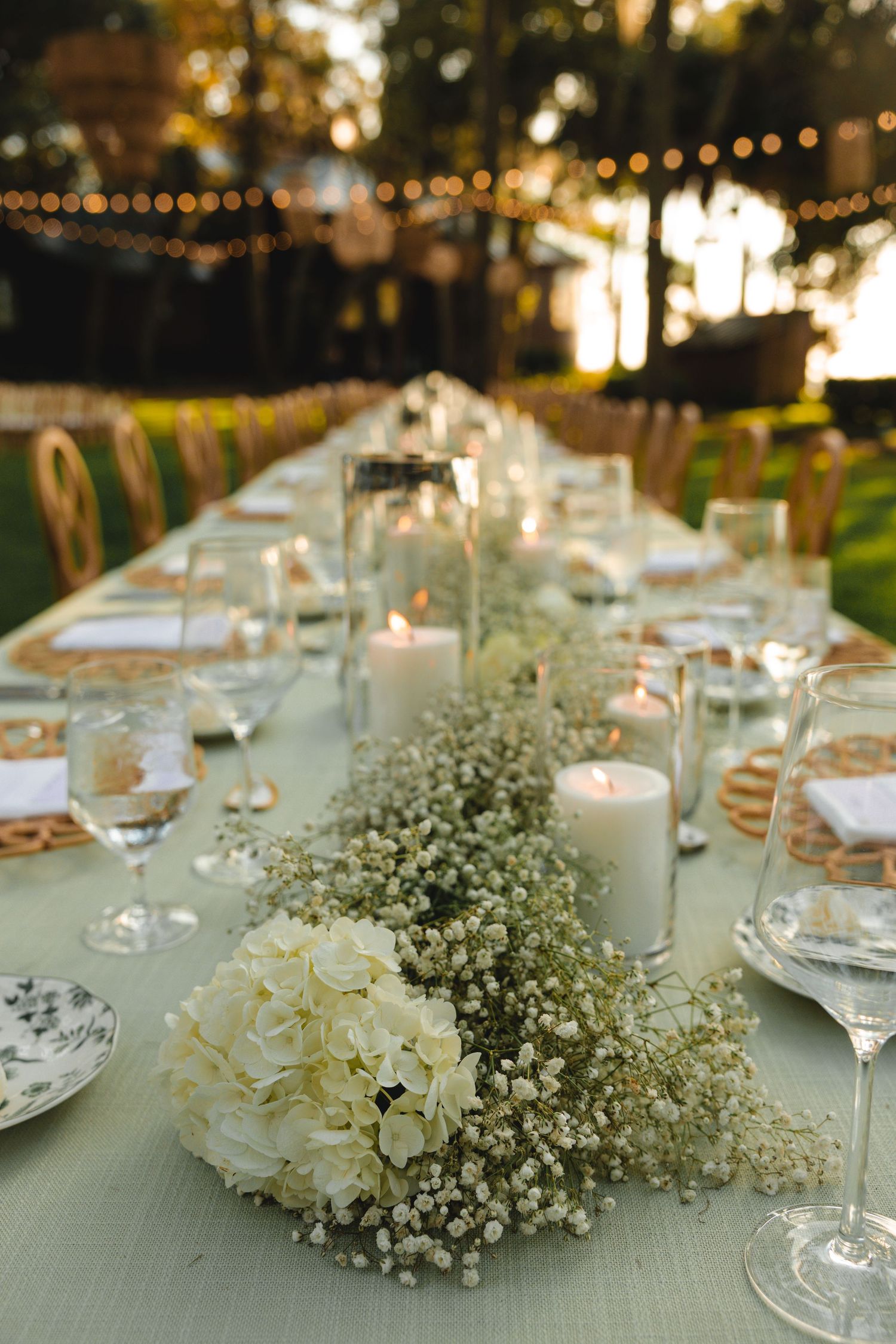 Elegant outdoor wedding table setting with baby's breath centerpieces and string lights at sunset.