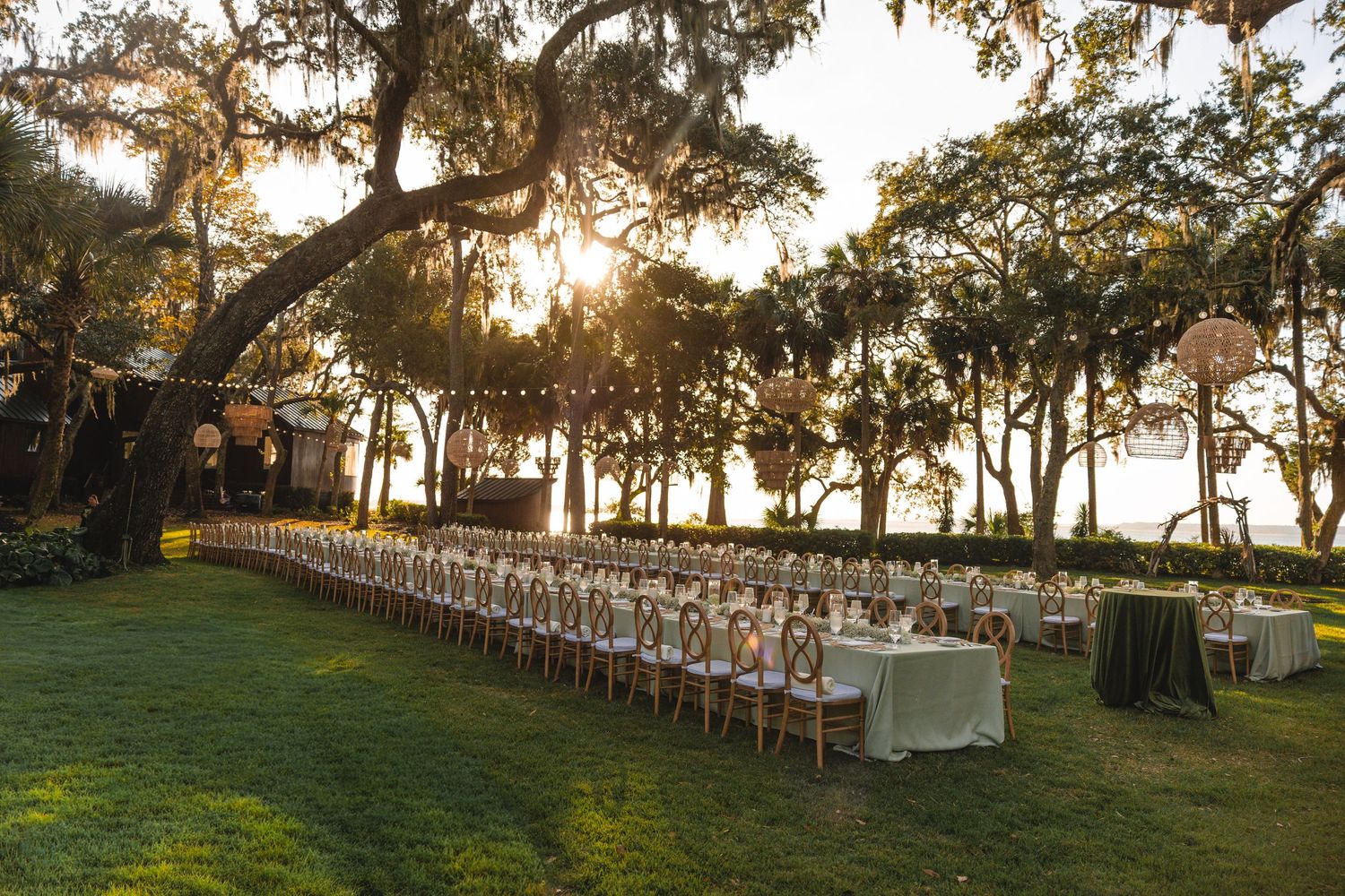 Long rows of white chairs set up for an outdoor wedding ceremony at sunset under oak trees.