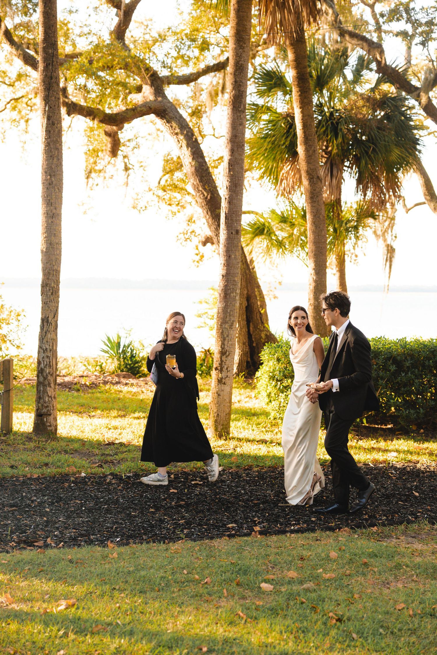 People gathered for an outdoor celebration under moss-draped oak trees in golden evening light.