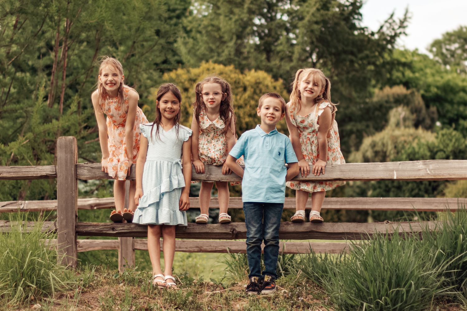 Kids sitting on a wooden fence in coordinated outfits during an outdoor photo session.
