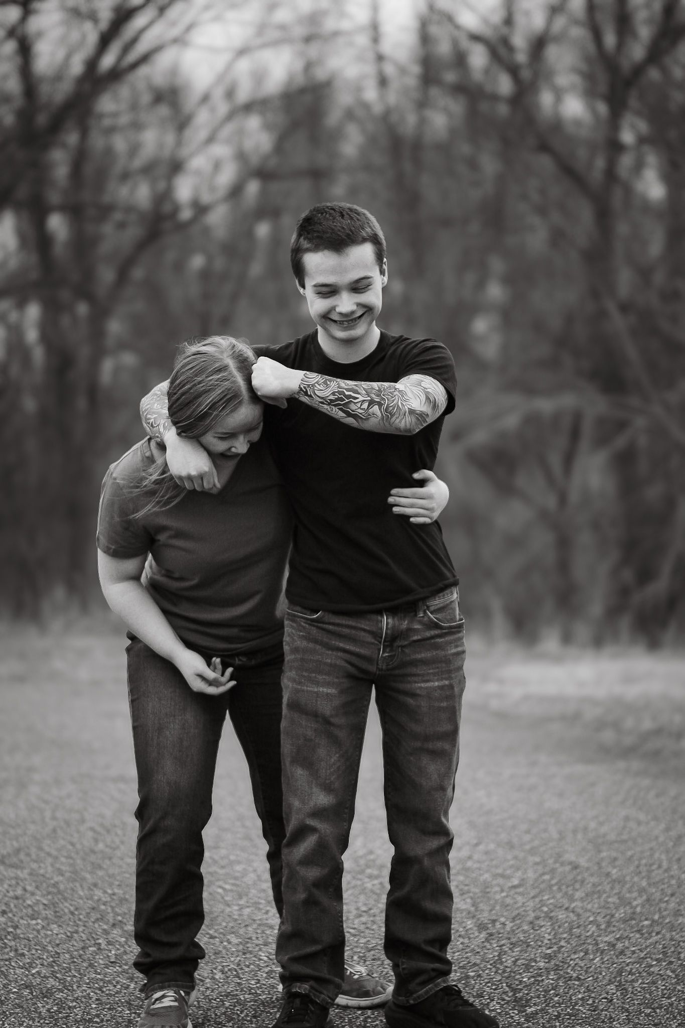 A candid black and white photo of two people sharing a lighthearted moment together outdoors on a path.