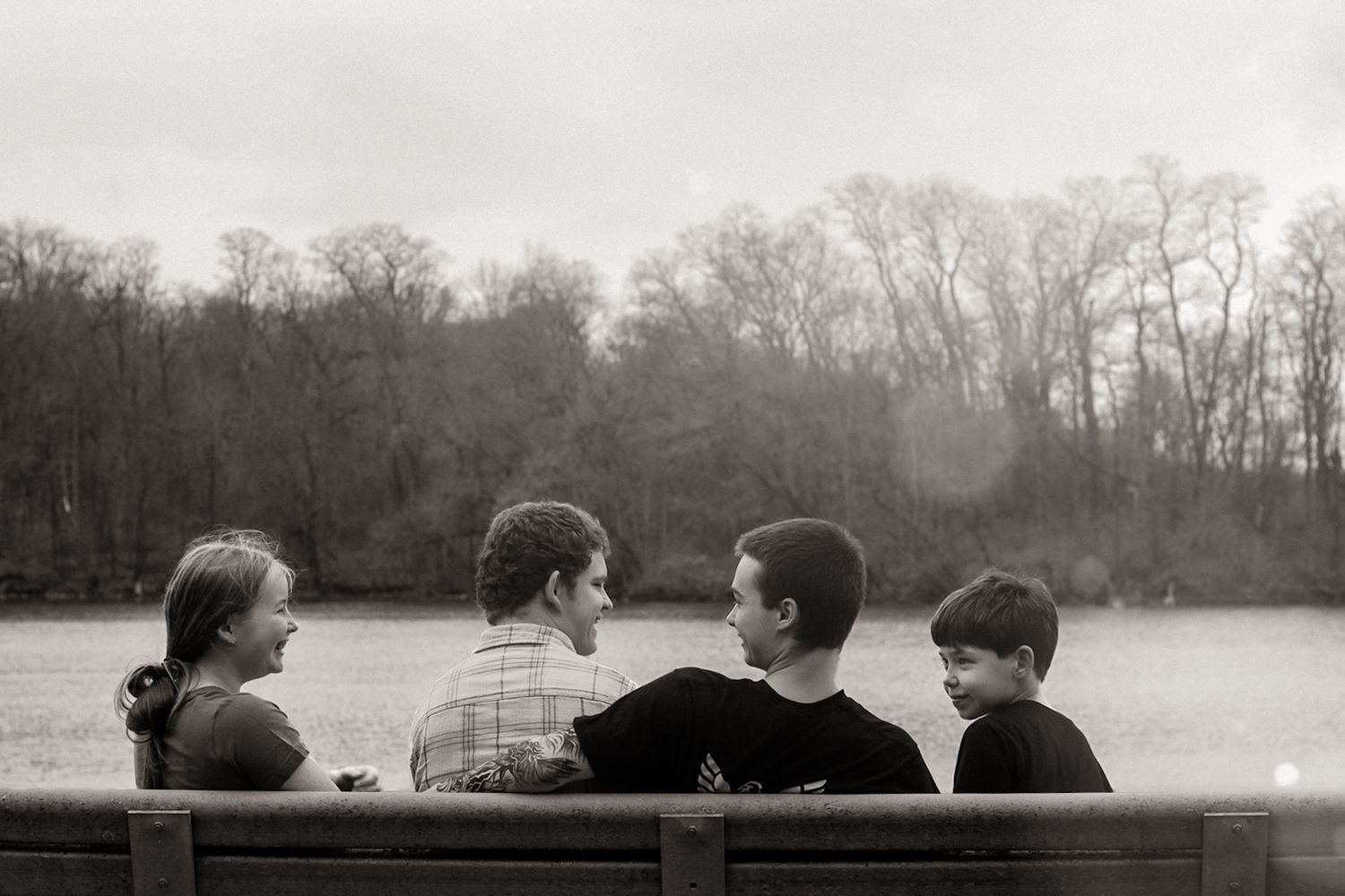A group sits together on a bench overlooking a lake in black and white, silhouetted against a misty treeline.