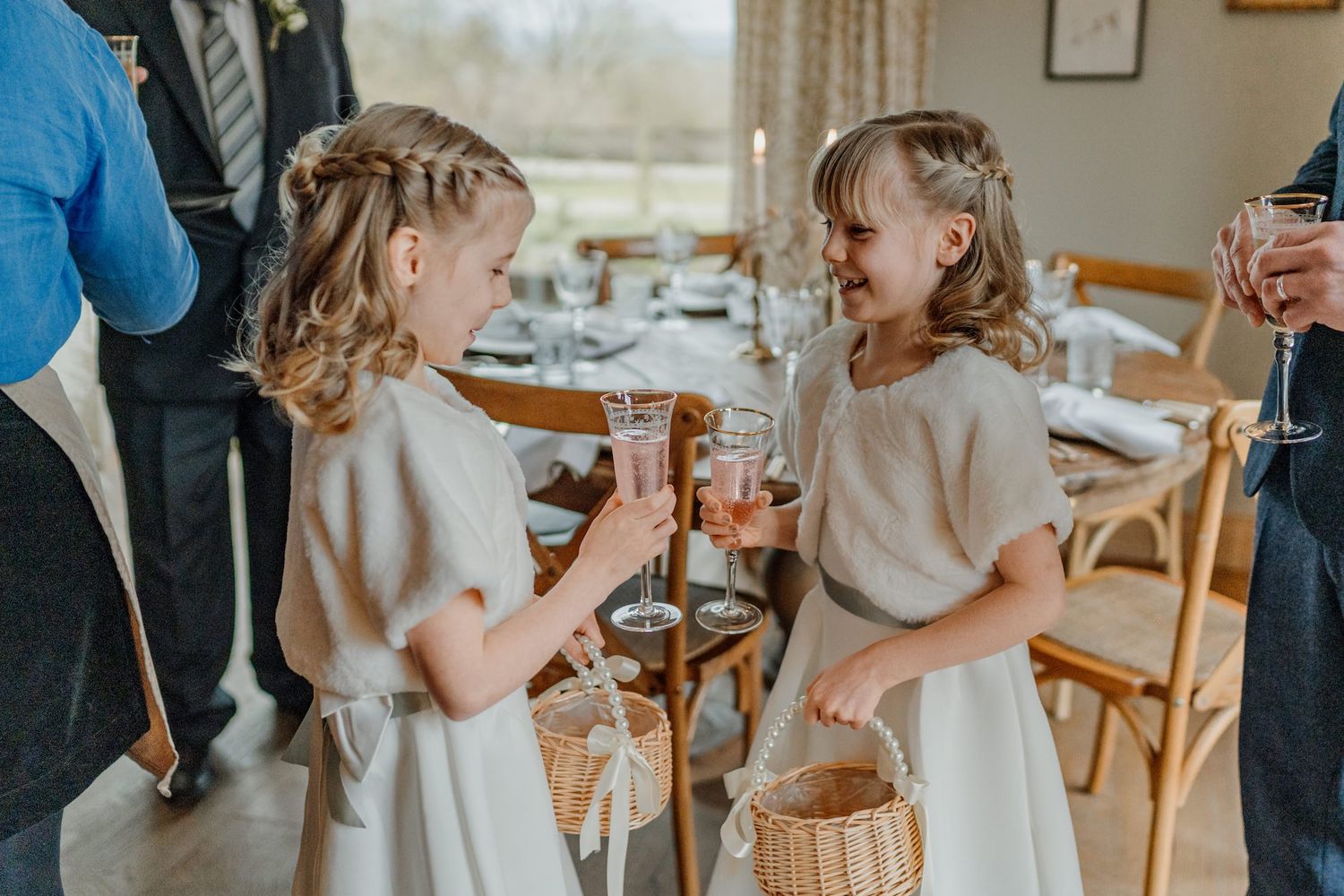 Young attendants in white dresses share playful moments during wedding preparations.