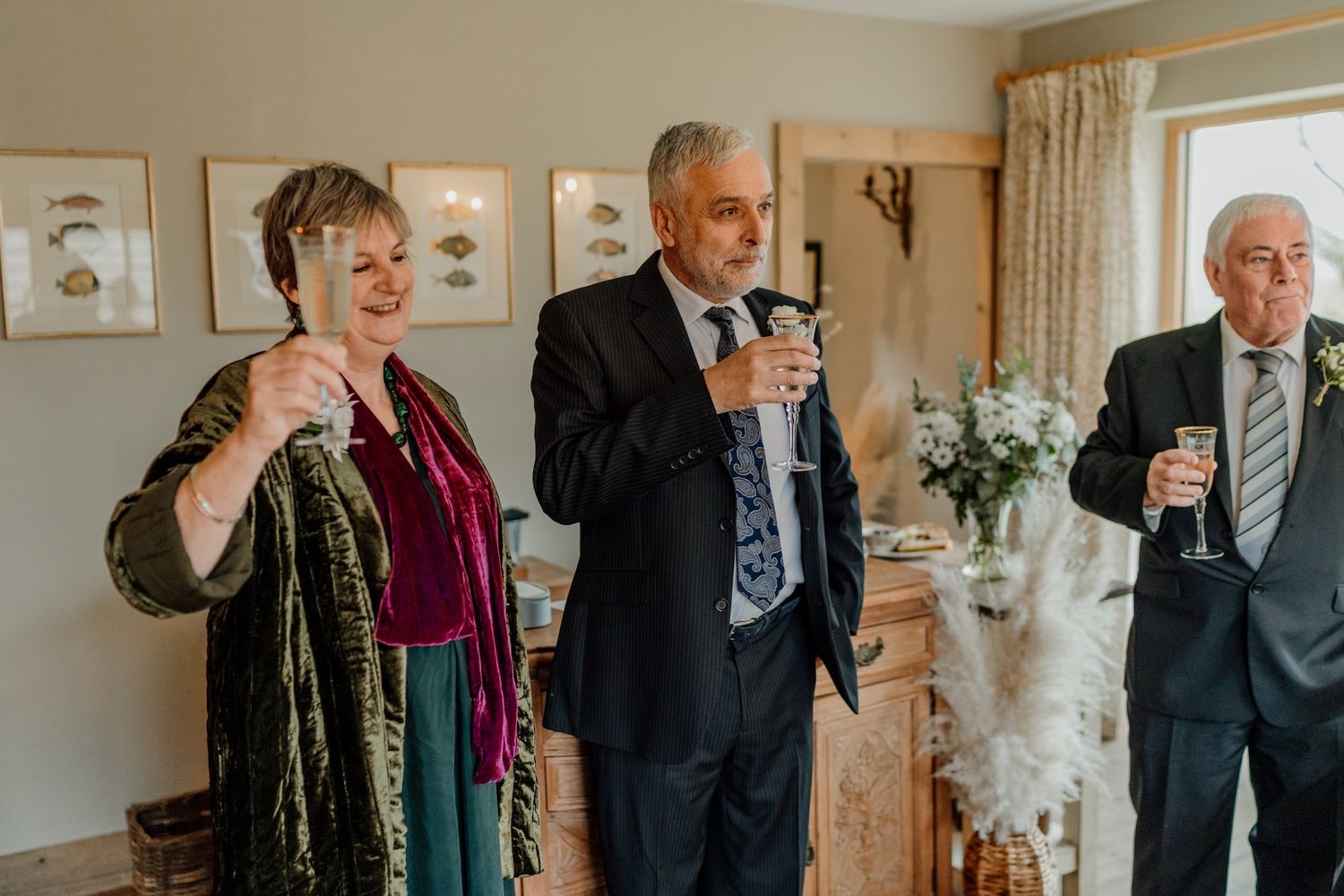 Guests raise champagne glasses in a toast during an elegant celebration in a sunlit room with floral arrangements.