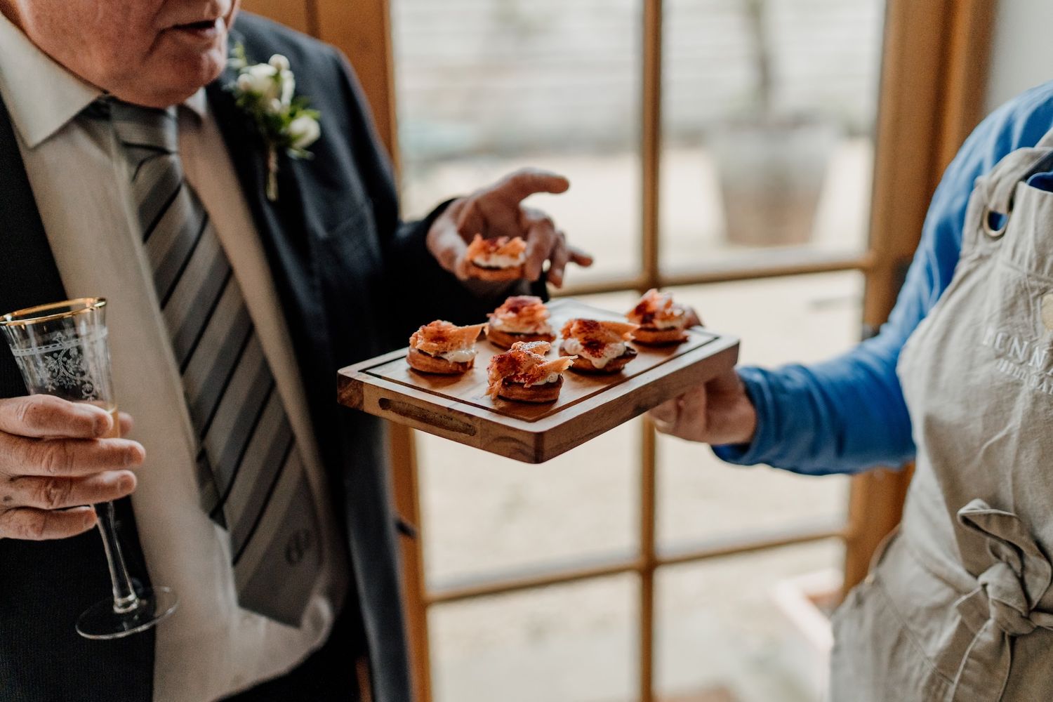 A tray of gourmet appetizers being served to guests holding champagne flutes at an elegant event.