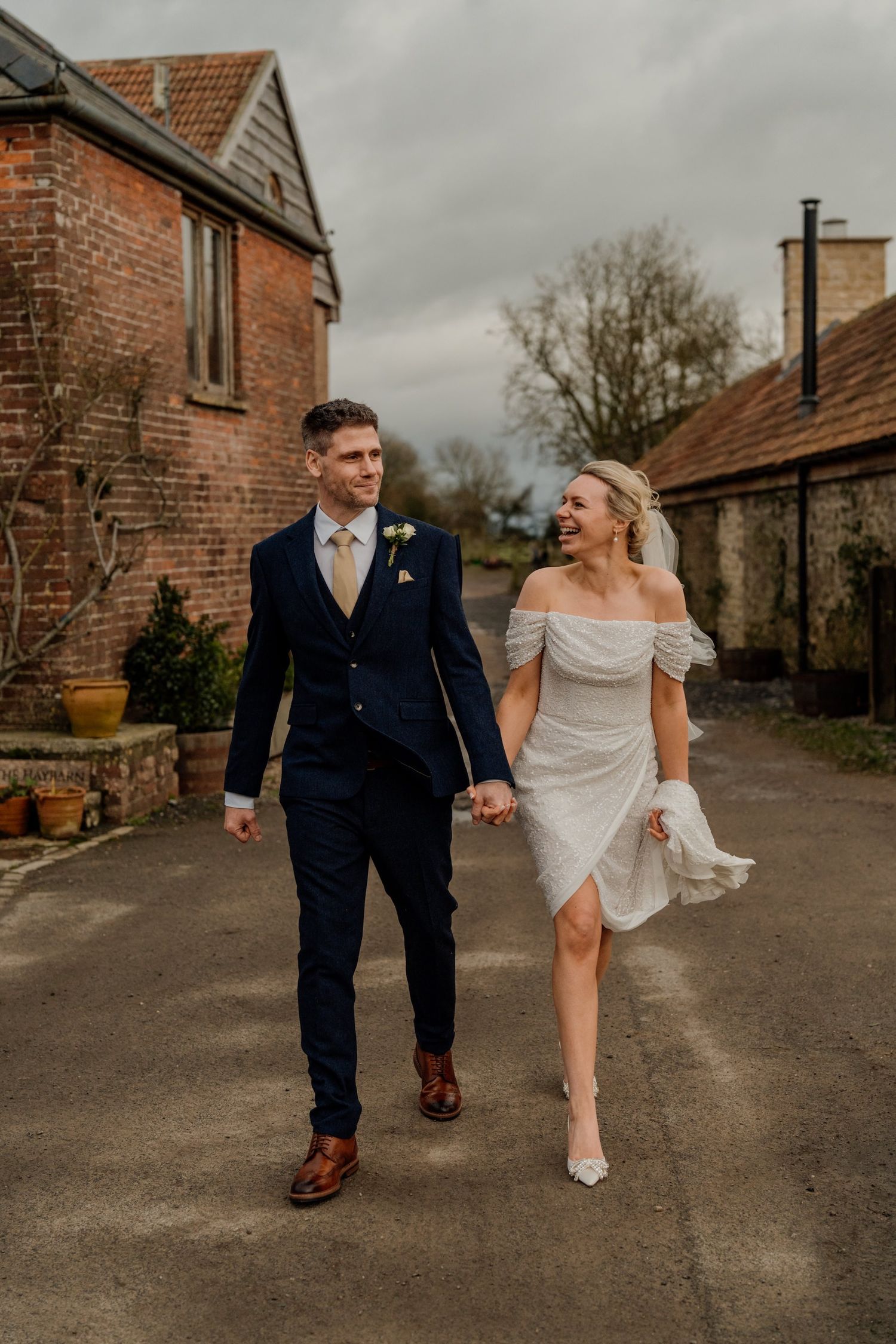 A newlywed couple walking together along a rustic brick path on their wedding day.