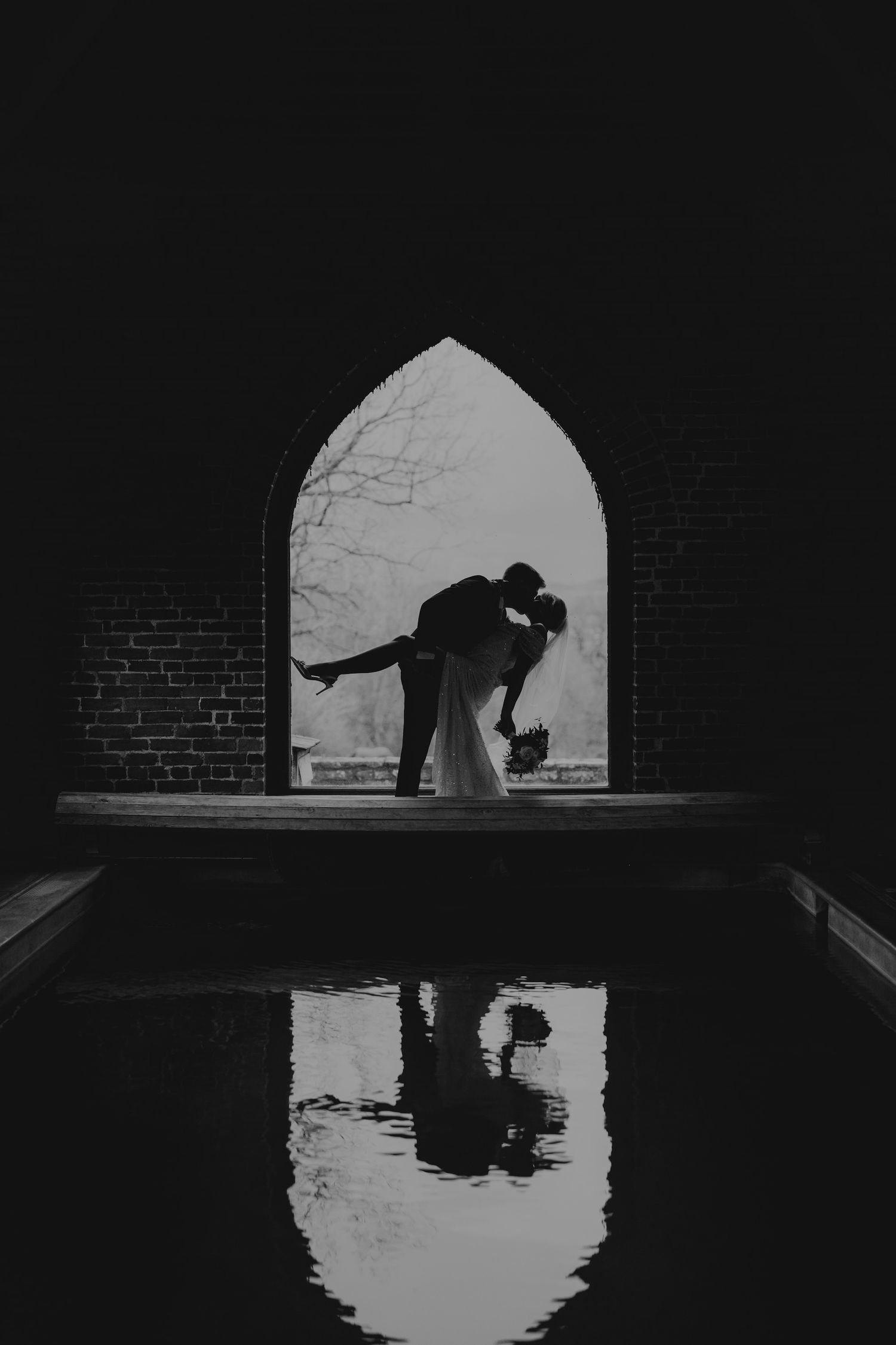Silhouetted figure and reflection in water creates dramatic black and white symmetry beneath arched brick tunnel.