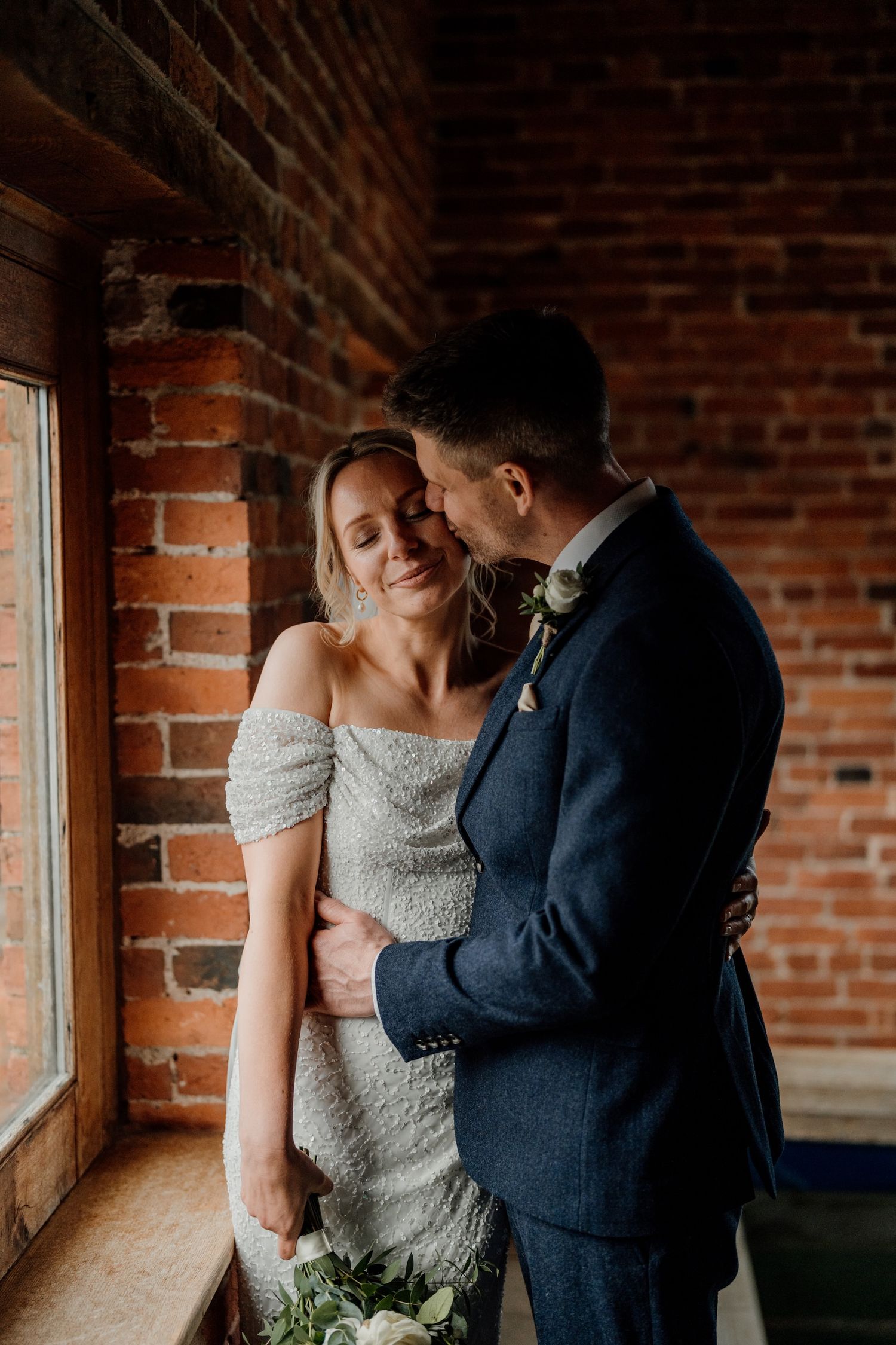 Couple shares intimate moments together in rustic brick venue with natural lighting streaming through windows.
