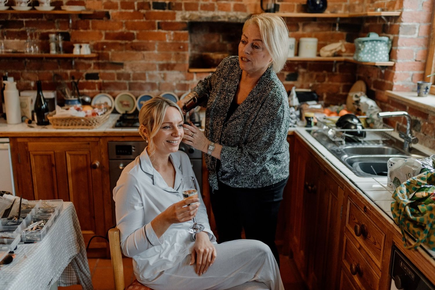Wedding preparations in a rustic brick-walled room as people gather around a dining table.