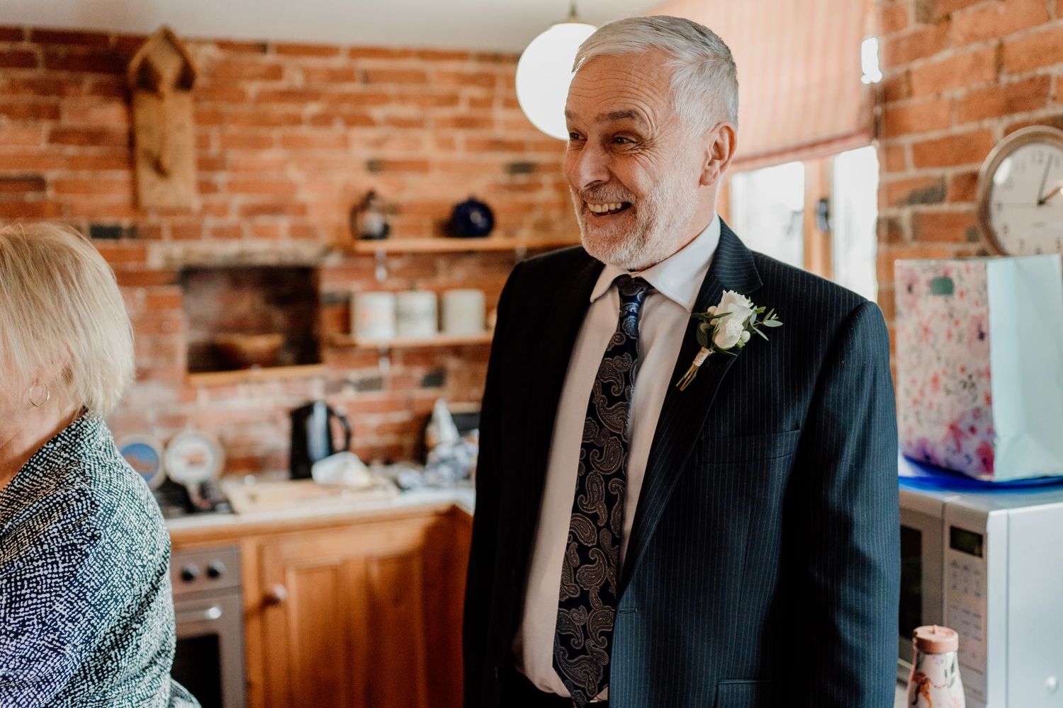 Wedding party members in formal attire share joyful moments in a rustic brick-walled space.