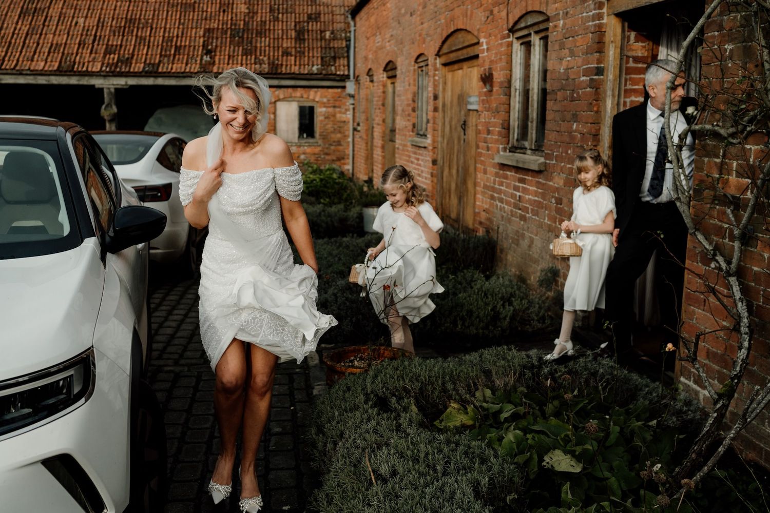 Wedding party walking along a brick building exterior pathway on a cloudy day.