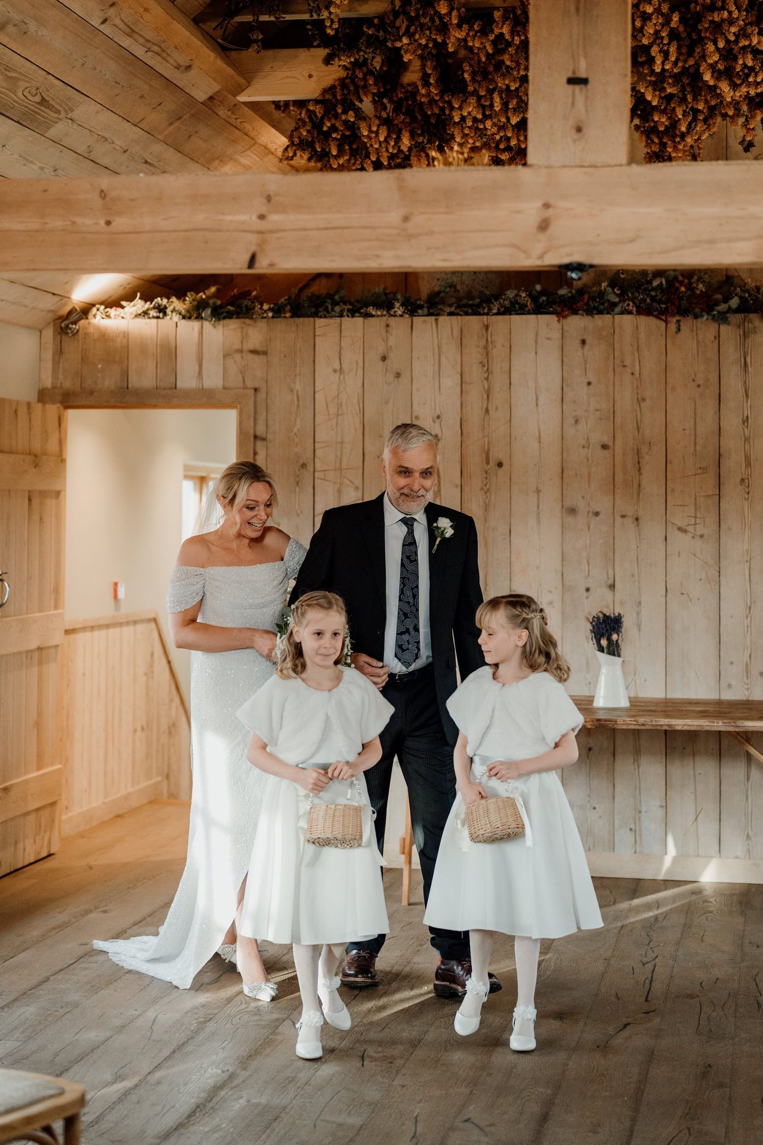 Wedding attendants in white dresses gather in a wooden barn-style room for photos.