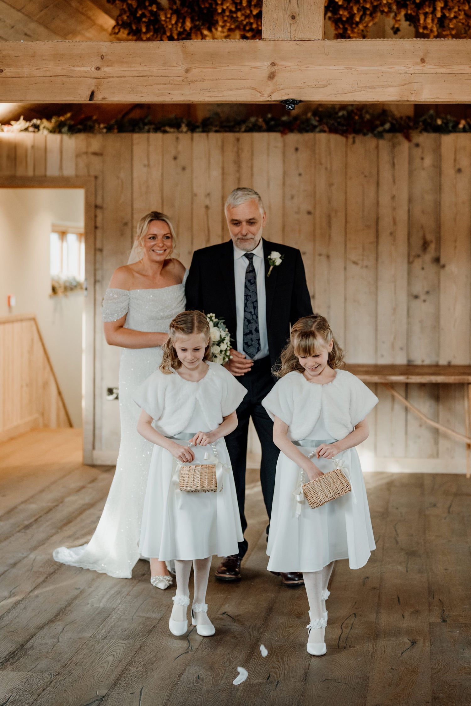 A group walks together in formal attire through a rustic wooden barn interior.