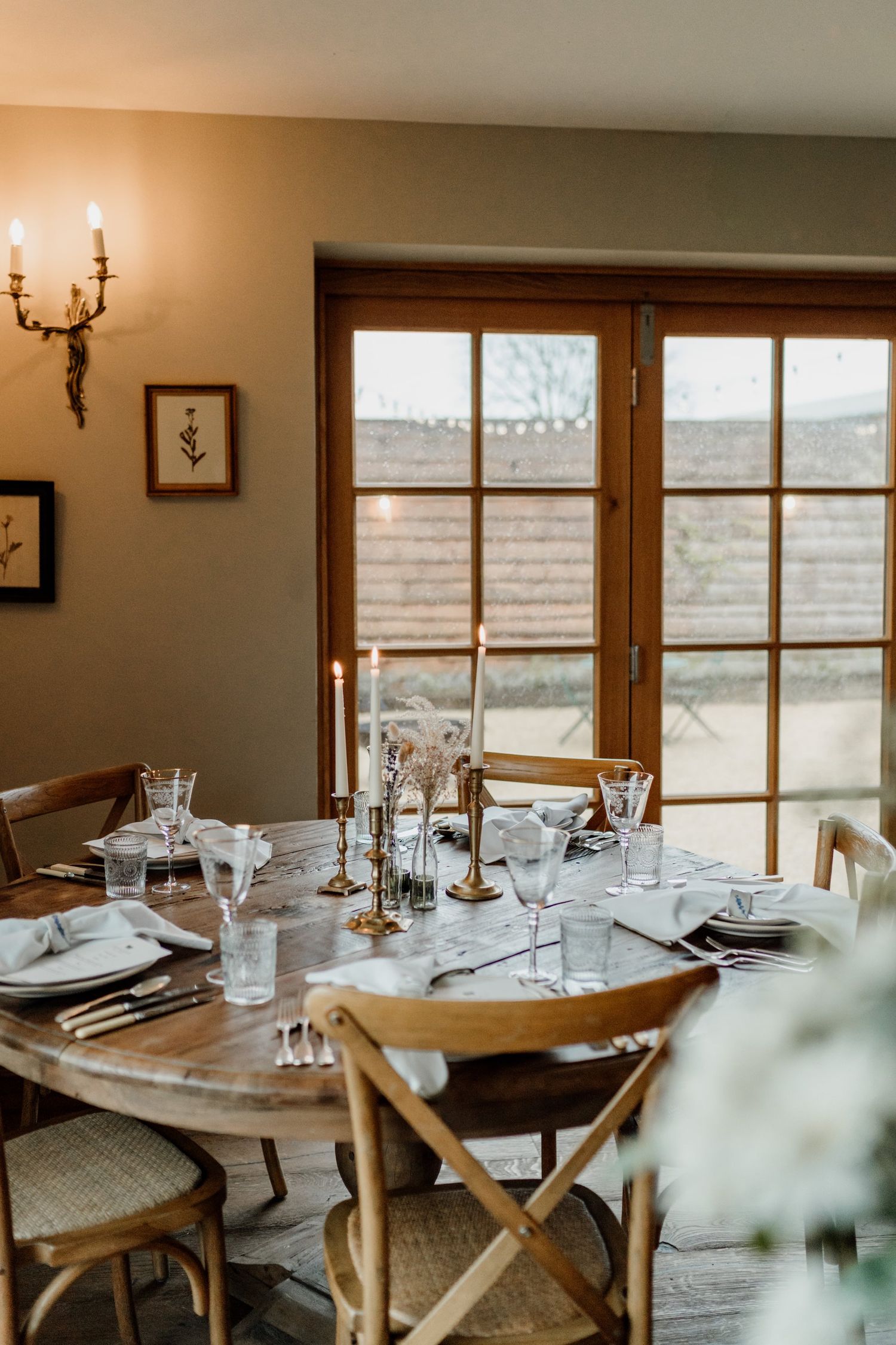 Elegant dining room setup with wooden tables, white tablecloths, and place settings in a rustic restaurant space.