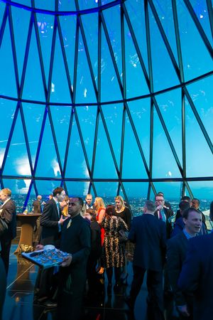 People gather in a modern event space with dramatic blue lighting and geometric glass ceiling architecture.