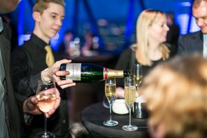 People enjoying drinks and socializing at a dimly lit bar with wine glasses and bottles visible in the background.
