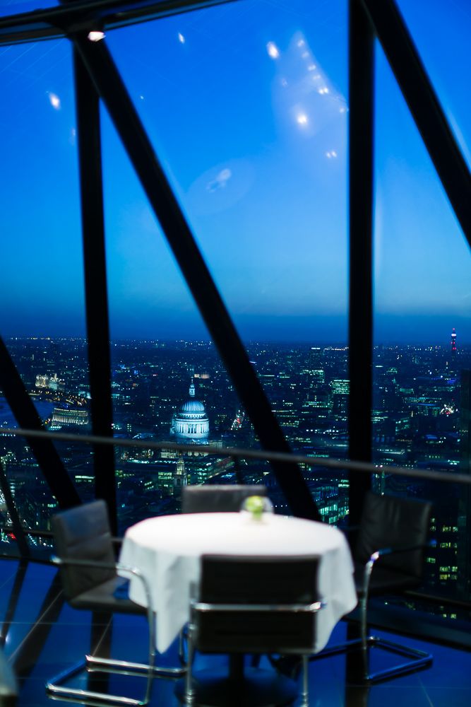 A romantic dining table set against floor-to-ceiling windows overlooking a glittering cityscape at night.