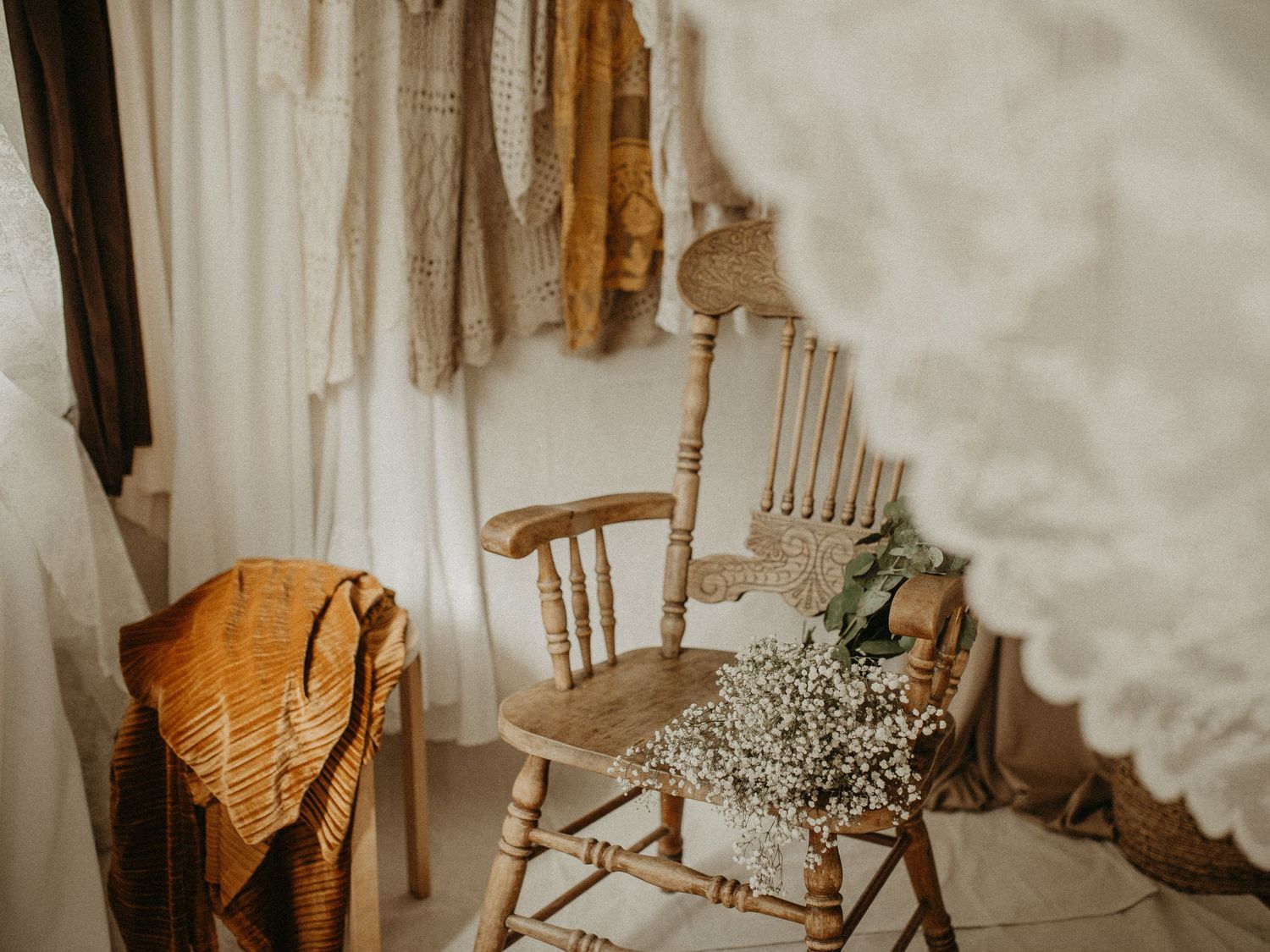 Elegant maternity gown hangs from wooden arch with baby's breath flowers and white curtains in rustic setting.