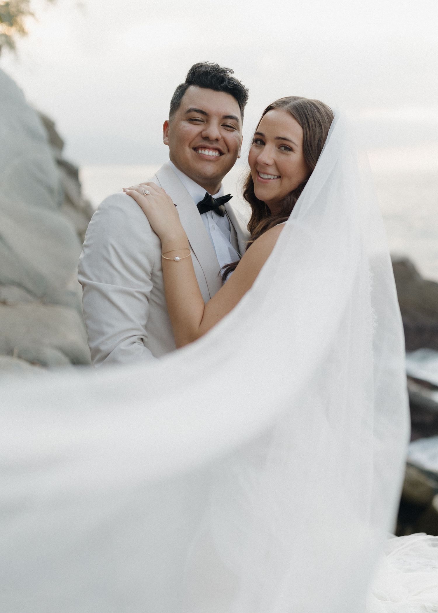 A married couple poses with the flowing white wedding veil catching in the breeze during an intimate Mexico wedding day.