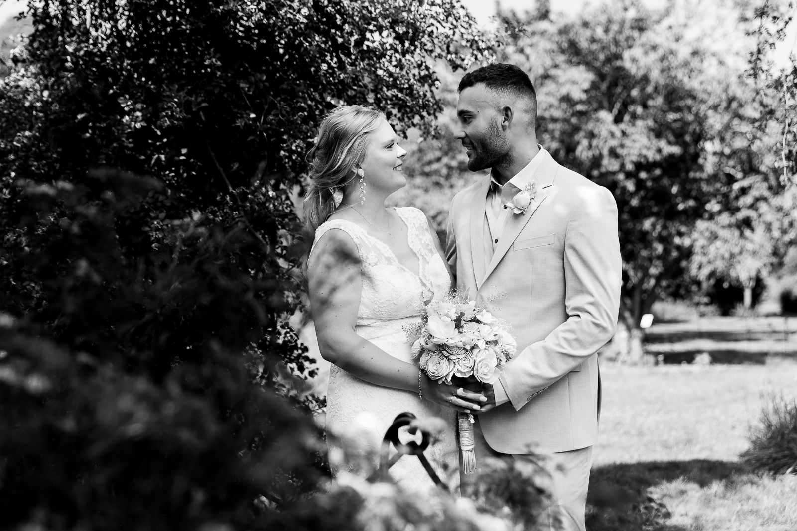 A couple in formal wedding attire share intimate moments in a sunlit garden setting during their marriage celebration.