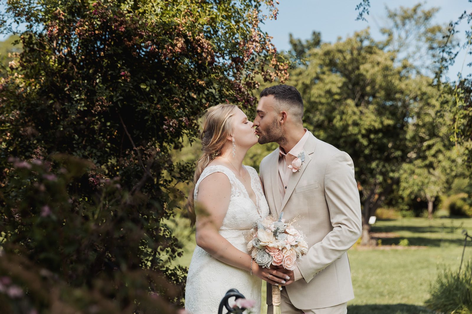 A romantic outdoor wedding photography session in a sunny orchard with a couple in white attire.