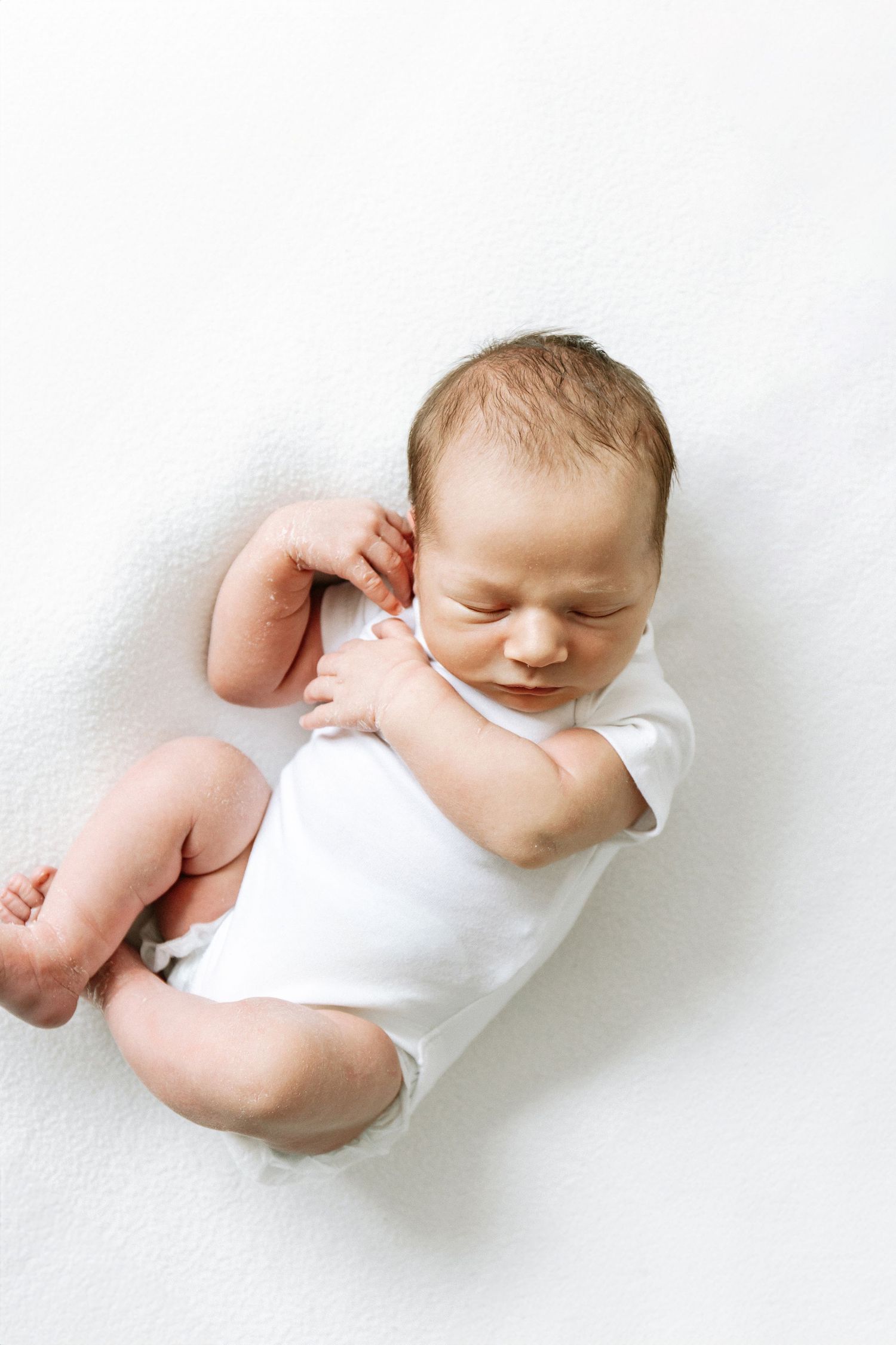 A sweet sleeping baby wearing white lies peacefully on a light background, during newborn shoot in Nottingham