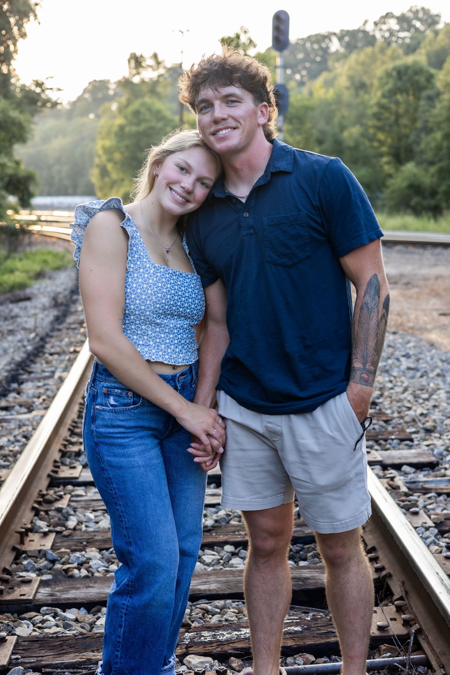 Couple posing playfully on train tracks in casual outfits during outdoor photo session.
