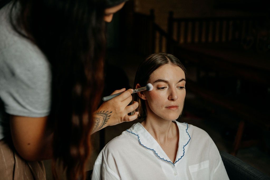 Makeup artist applying foundation to bride's face during wedding morning preparations.