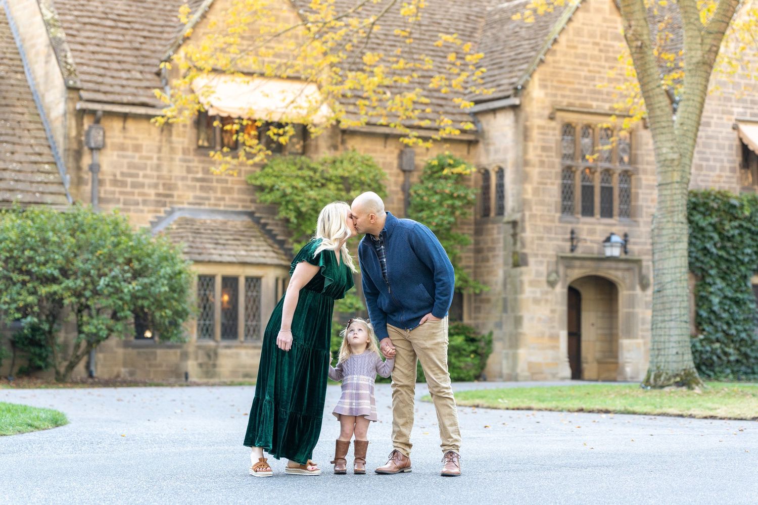 Family standing together outdoors in front of a stone building with autumn foliage.
