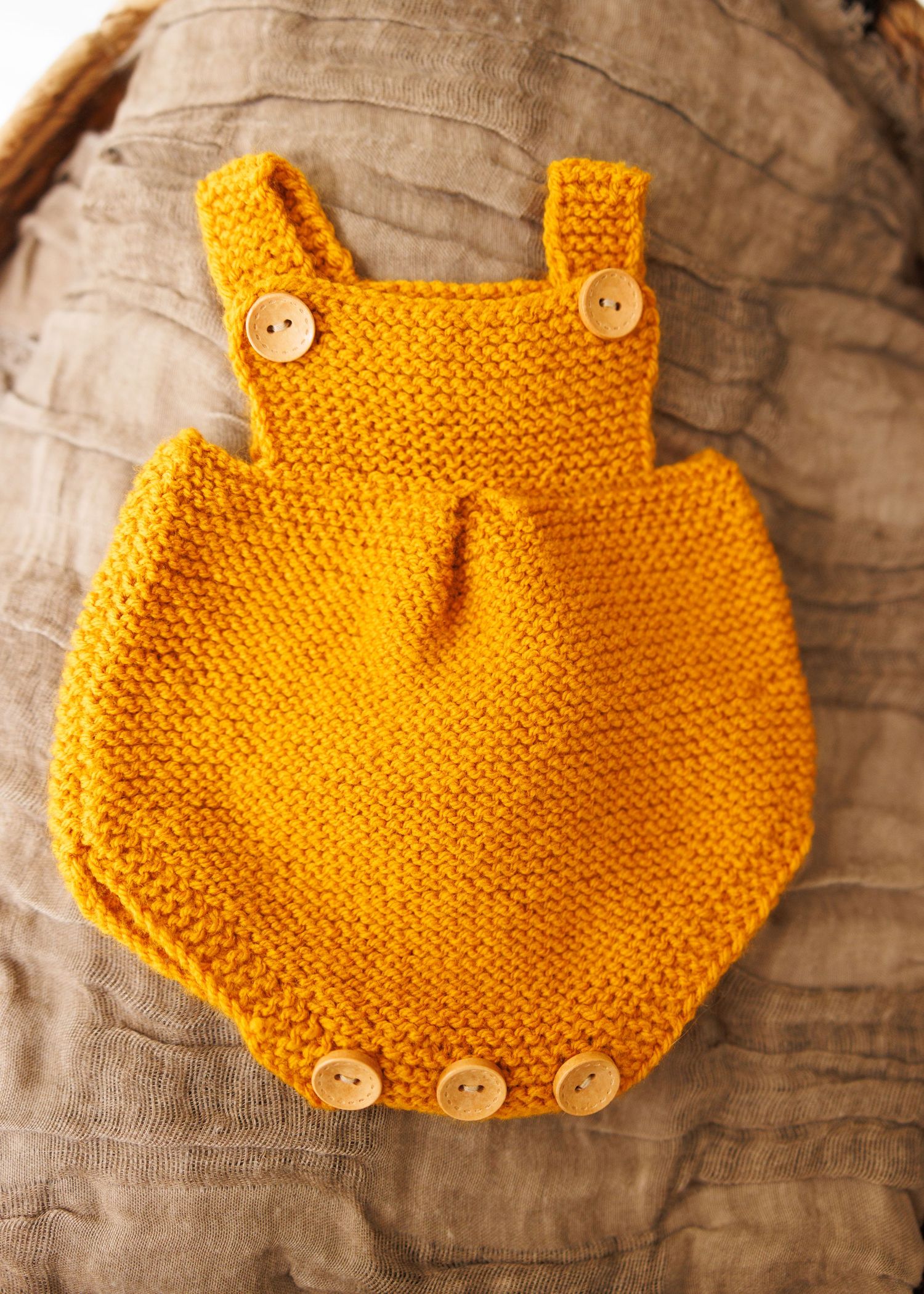 Vintage knitted baby bonnet with lace trim and ties rests on delicate crocheted doily background in neutral beige tones.