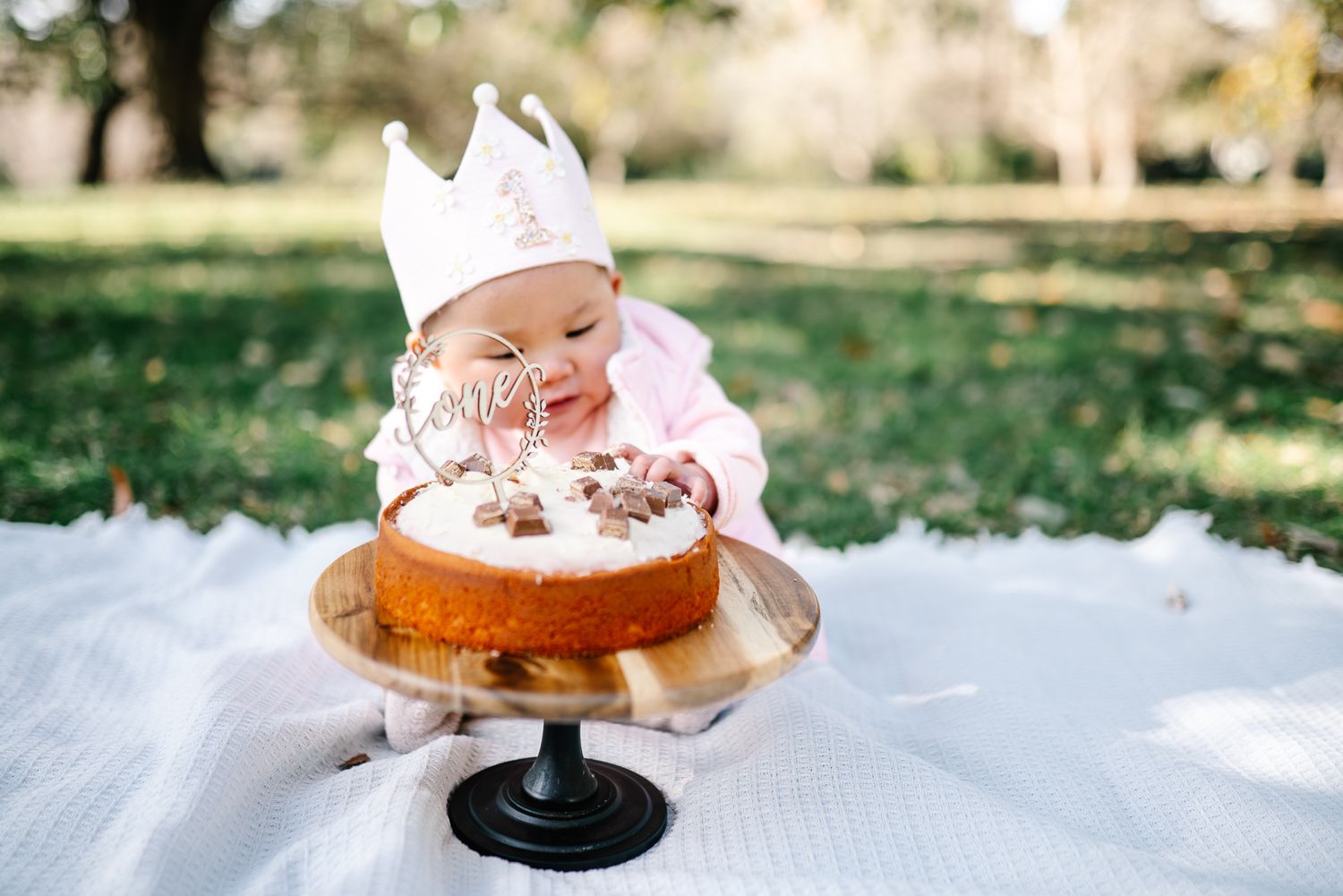 Baby reaches excitedly for a vanilla-frosted donut with pink sprinkles for her first birthday cake smash photography in Melbourne.
