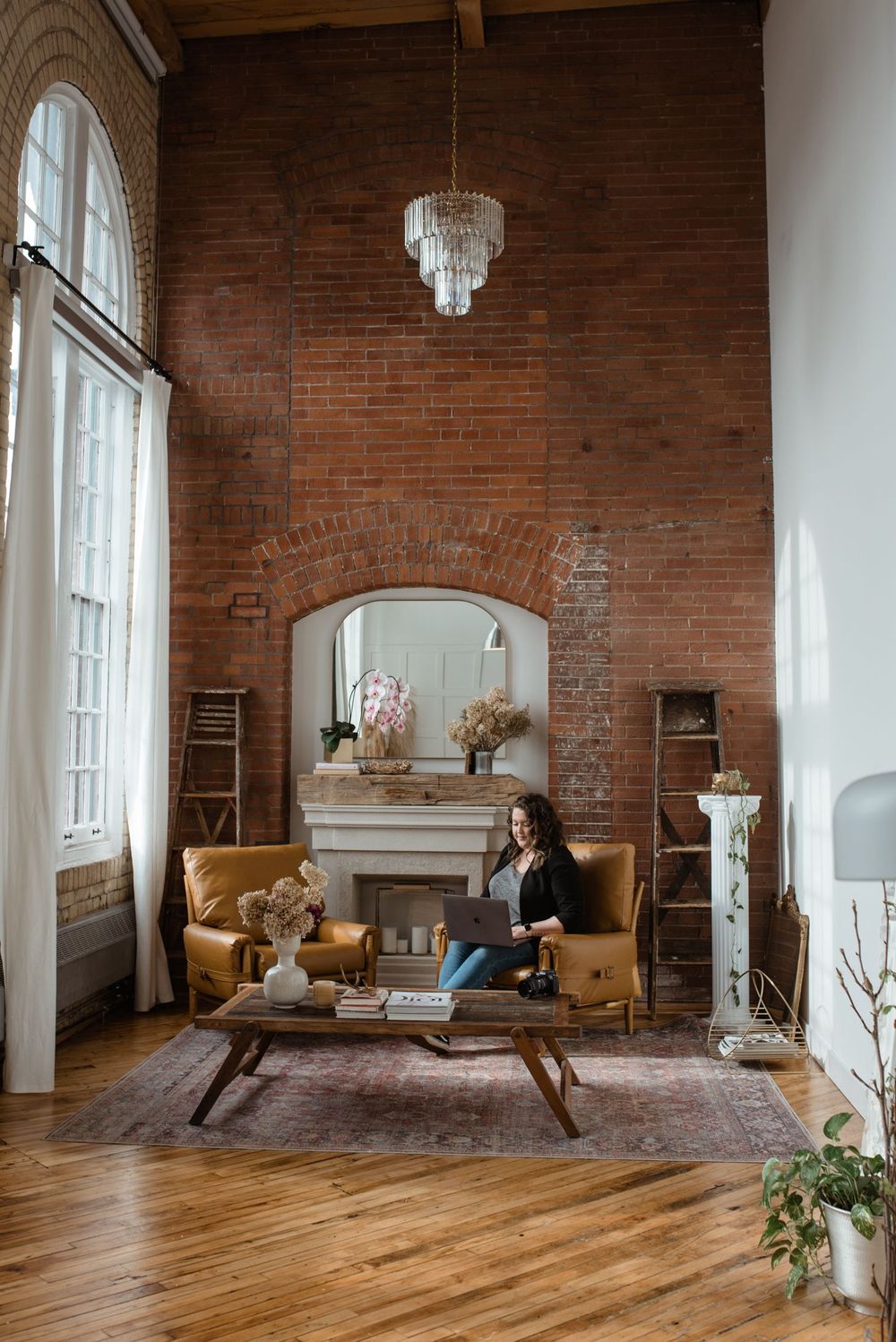 Cozy living room with exposed brick walls, crystal chandelier, vintage yellow sofa and hardwood floors.