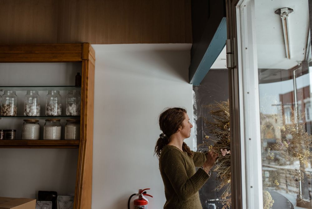 An artisan working in a rustic kitchen space with glass jars on wooden shelves in the background.