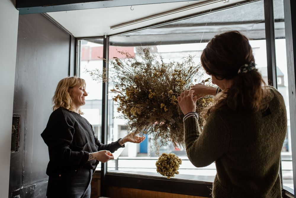 Two people working together in an artisan studio arranging dried floral arrangements.