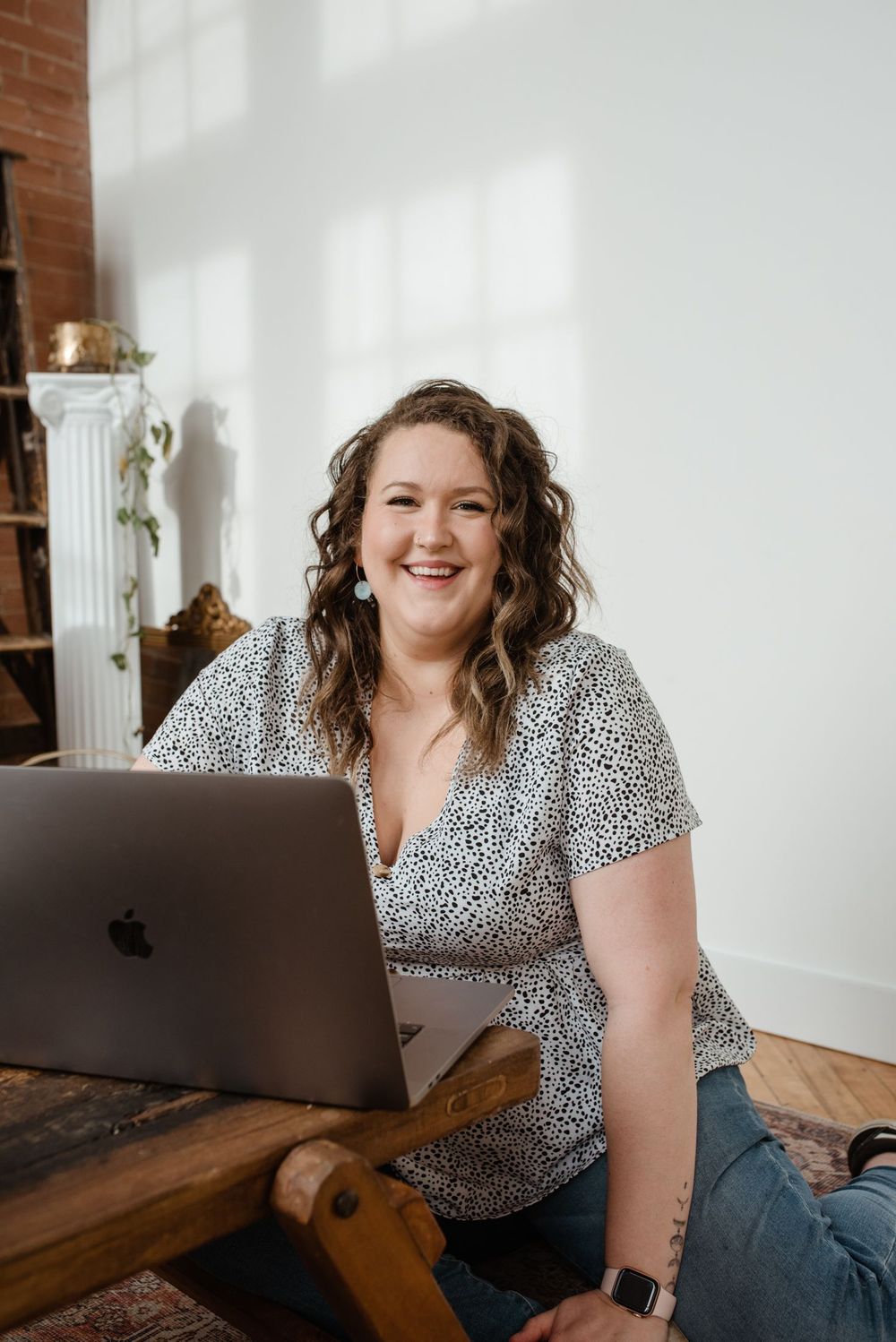 Someone in a leopard print top smiling while working on a MacBook laptop on a wooden table.