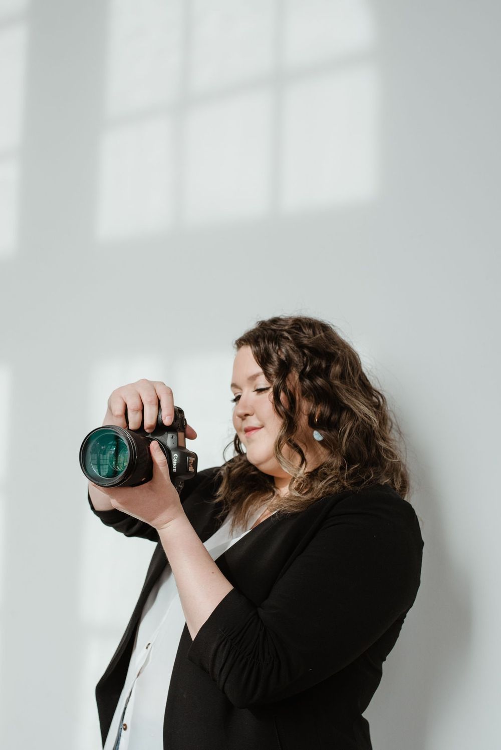 Professional photographer adjusting camera settings against white wall with dramatic window shadows.
