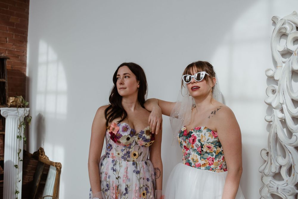 A group of friends in floral dresses laughing and posing together in a bright studio space.