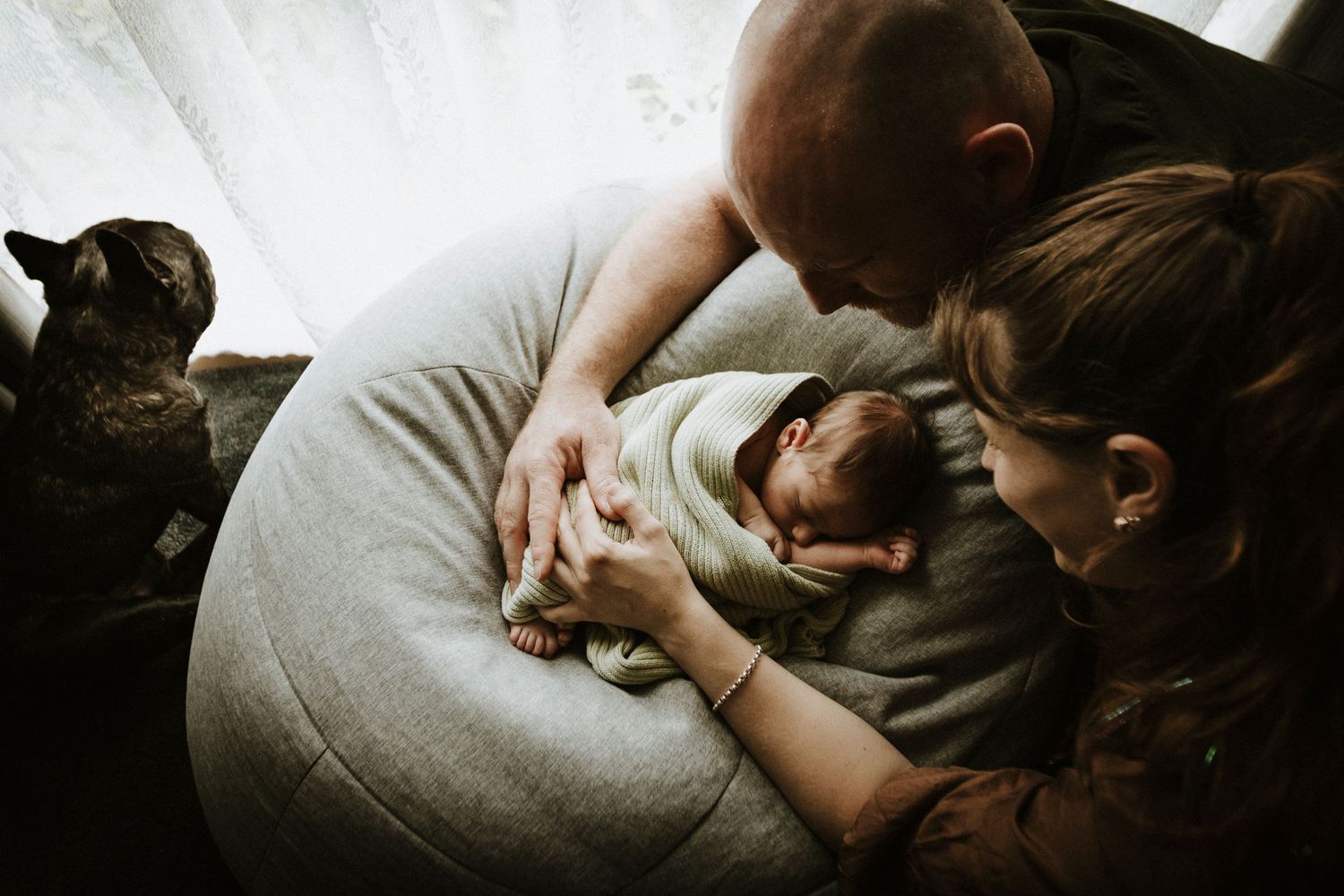 Atmospheric photos showing intimate emotional moments between parents and their newborn in low light.