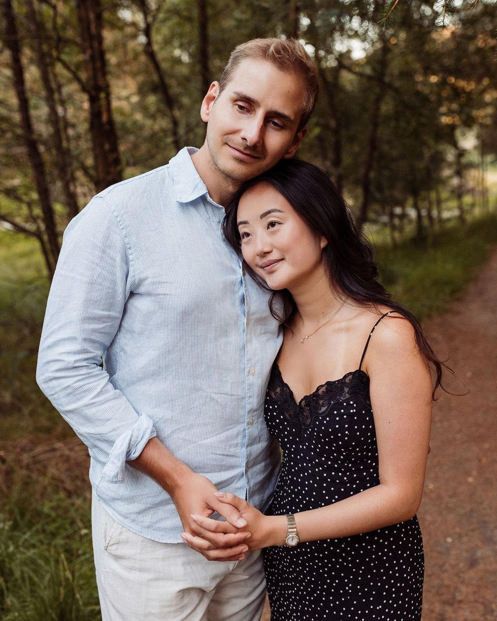 A romantic couple embraces while standing together on a forest path during a golden autumn afternoon.