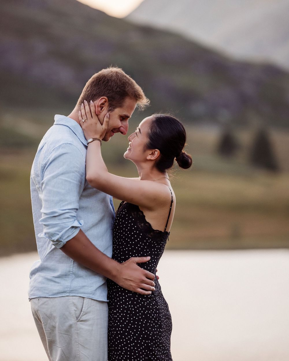 Couple in white shirt and polka dot dress share intimate moments during sunset photoshoot in outdoor landscape.