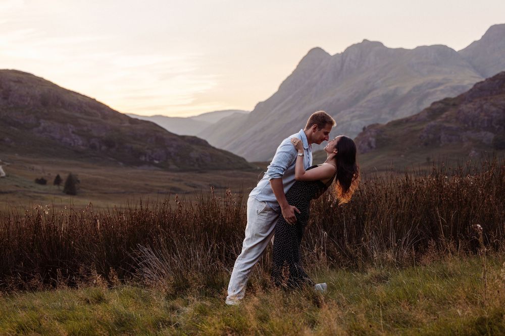 A couple embraces and kisses in silhouette against a dramatic mountain landscape at sunset.