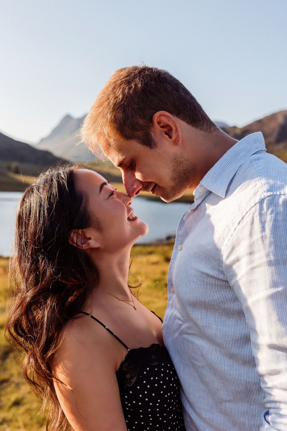 A romantic couple shares an intimate moment in front of a scenic mountain lake during golden hour.
